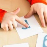 Afbeelding van child using paint to create letter shapes on paper